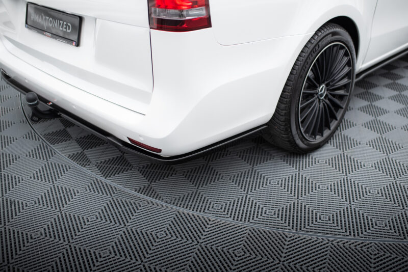 Rear view of a white car showing the tail light, curved bumper, and a tow hitch on a patterned floor surface.