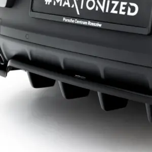 Close-up of a dark car rear bumper with dual exhaust pipes and a blurred license area showing the text '#MAXONIZED' and 'Porsche Centrum Rzeszów'