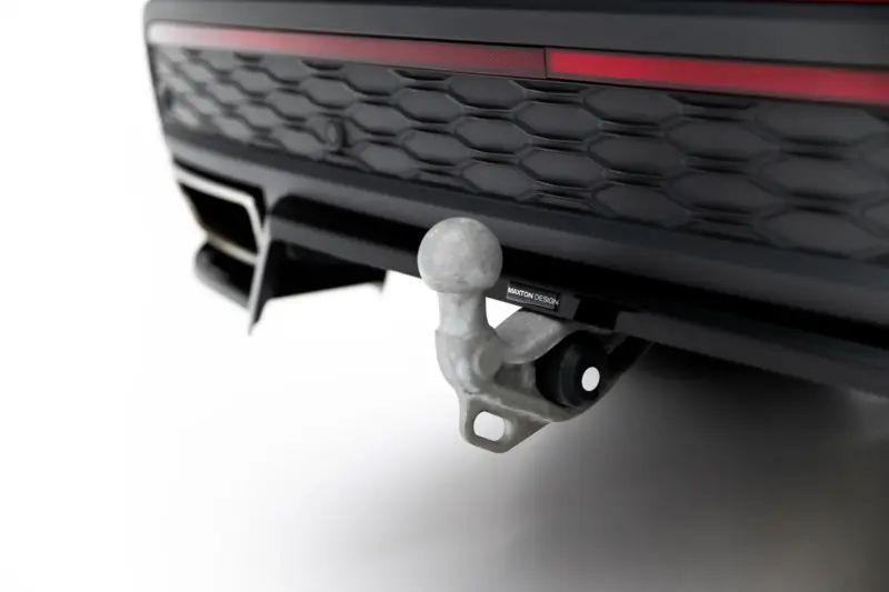 Close-up of a tow hitch ball attached to a vehicle's hitch beneath the front bumper and grille with a red accent light behind.