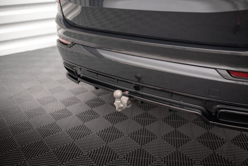 Rear view of a dark car showing a tow hitch ball attached to the bumper in a showroom setting.