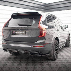 Rear three-quarter view of a dark gray Volvo SUV in a bright studio with striped walls; tail lights and license plate reading '#MAXTONIZED' visible.