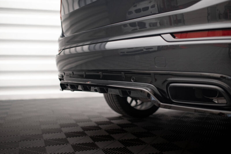 Close-up of the rear end of a glossy black car, showing the taillight strip and lower bumper on a showroom floor.