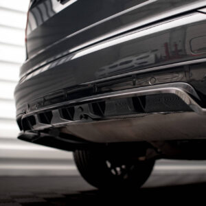 Close-up of a shiny black car rear bumper, showing the chrome trim and exhaust area in the lower rear