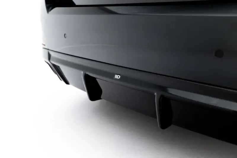 Close-up of a dark car rear bumper with a small rectangular badge visible near the center bottom of the image.