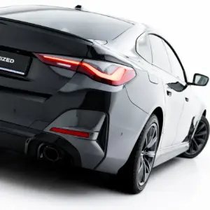 Rear three-quarter view of a black BMW showing taillight, exhaust, and the '#MAXTONIZED' plate badge on a white backdrop.