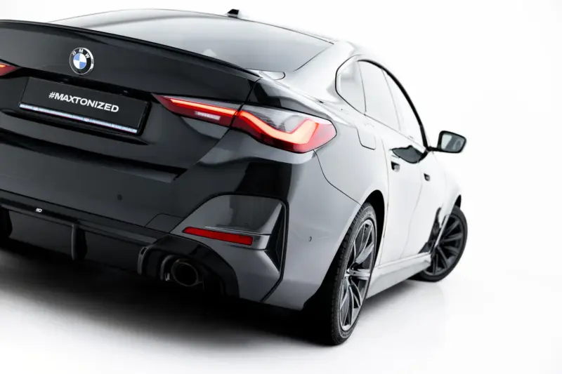 Rear three-quarter view of a black BMW showing taillight, exhaust, and the '#MAXTONIZED' plate badge on a white backdrop.