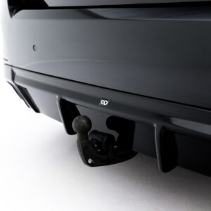 Close-up of a car’s rear hitch with a round trailer ball and mounting plate visible on a dark bumper area.