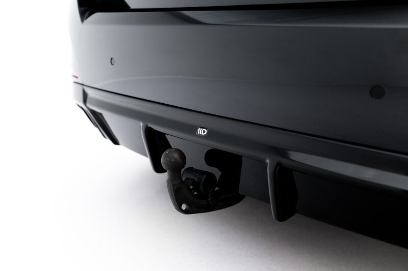 Close-up of a car’s rear hitch with a round trailer ball and mounting plate visible on a dark bumper area.