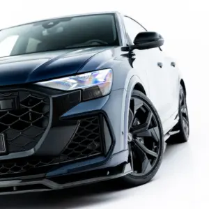 Close-up of a dark blue Audi front end with honeycomb grille and sharp headlight, angled to the left (showing the logo area)