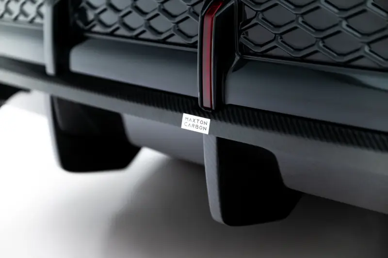 pol_po_Set-of-Prepreg-Carbon-Fiber-Splitters-Audi-RSQ8-Mk1-Facelift-23818_4webp - OPSHOLDERS Close-up of a black car front bumper with carbon fiber accents and a Maxton Carbon badge.