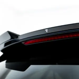 Close-up of a car spoiler with carbon-fiber texture and a red taillight, set against a white background.