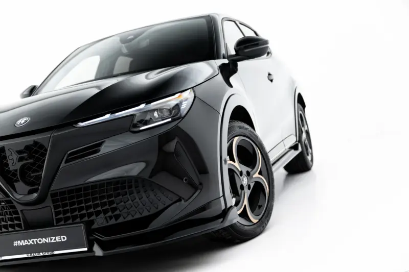 Close-up of a black sports car's front end, showing the glossy hood, LED headlight, and wheel with a branded badge.