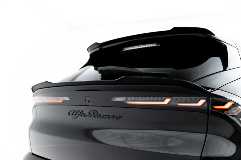 Rear view of a sleek black Alfa Romeo car with glowing red taillights and visible logo on the trunk.