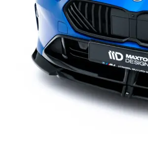 Close-up of a blue car's front bumper and black grille with a Maxton Design license plate badge visible on the right side