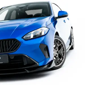 Front-left angled view of a blue BMW with a black grille, headlight, and alloy wheel; Maxton Design plate visible on the bumper.