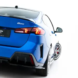 Rear view of a blue BMW showing the '220' badge and Maxton Design plate on a white background, illuminated tail lights visible.
