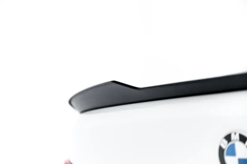 Close-up of a white car showing a black roof trim and the BMW emblem on the trunk.