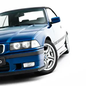 Blue BMW car prominently shown from the front-left, featuring the grille, headlight cluster, wheel, and a #MAXTONIZED license plate.