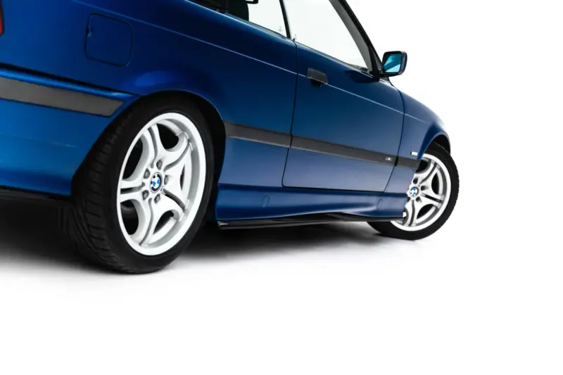 Blue BMW car shown from a low angle, highlighting the front wheel and side panel.