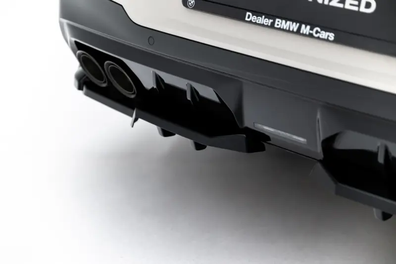 Close-up of the rear bumper of a dark BMW car, showing twin exhaust tips and a sporty diffuser.