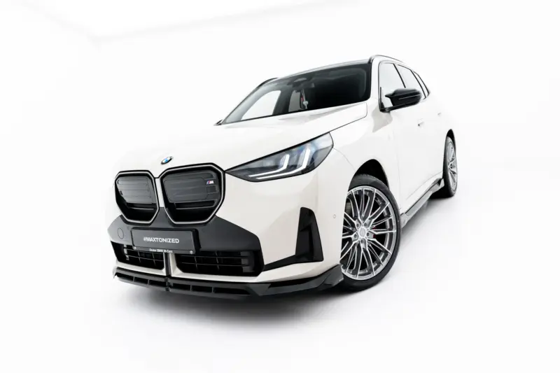White BMW M car angled from the front in a bright studio, showing the grille, headlights, and large alloy wheels.