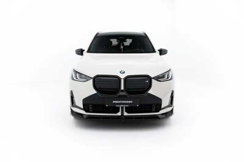 Front view of a white BMW SUV in a bright studio, showing the prominent kidney grille, LED headlights, and black lower bumper with a #MAXTONIZED license plate.