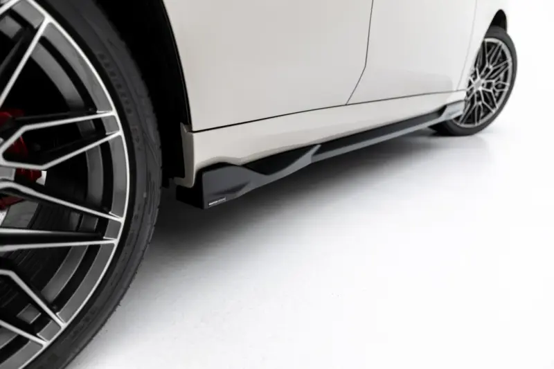 Close-up side view of a white car showing the lower body panel and a multi-spoke alloy wheel on a clean studio floor