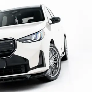 Close-up of a white BMW SUV front-left, showing the grille, headlight, and alloy wheel; license plate reads #MAXTONIZED.
