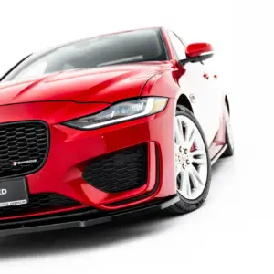Close-up angled view of a red Jaguar sports car showing the front grille, headlight, and wheel against a white background.