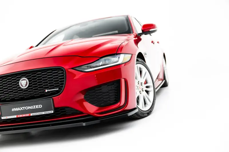 Close-up angled view of a red Jaguar sports car showing the front grille, headlight, and wheel against a white background.