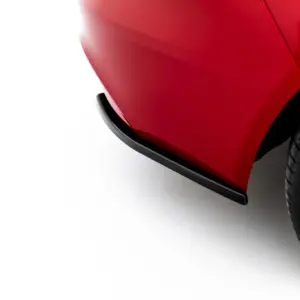 Close-up of a red car body near the front wheel, showing glossy paint and curved panels on a light surface