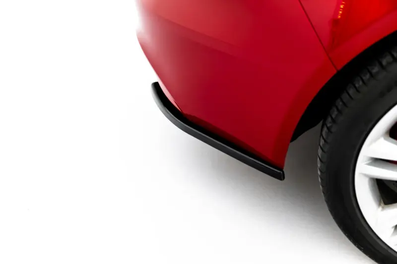 Close-up of a red car body near the front wheel, showing glossy paint and curved panels on a light surface