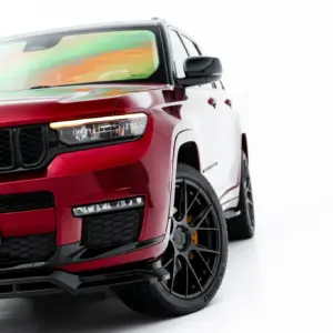 Close-up, front-left view of a red Jeep SUV showing the black grille, headlight, and glossy paint.