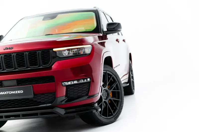 Close-up, front-left view of a red Jeep SUV showing the black grille, headlight, and glossy paint.