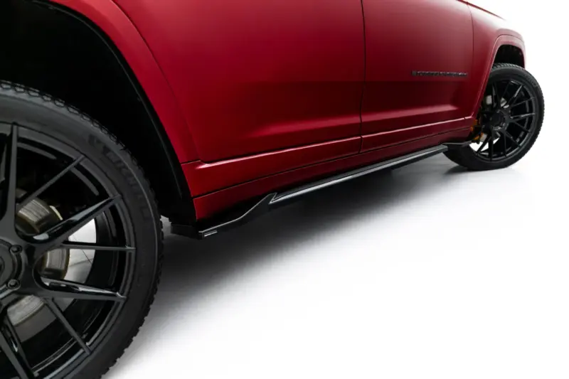 Close-up side view of a red Jeep Grand Cherokee, showing the front wheel, lower body line, and side step along the rocker.