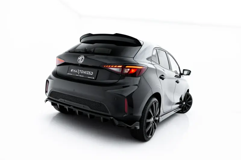 Rear view of a dark MG hatchback with a prominent rear spoiler and illuminated taillights against a white studio backdrop, showing MG logo on the trunk.