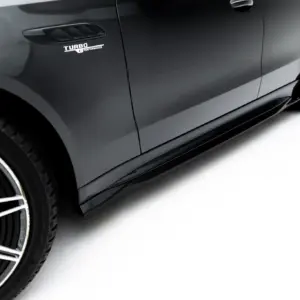 Close-up of a dark gray car side showing a 'Turbo Performance' badge near the front fender and a stylish alloy wheel with low-profile tire on a white background.