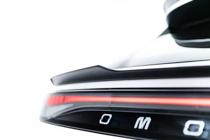 Close-up of a black car's rear taillight with a red LED strip against a white background.