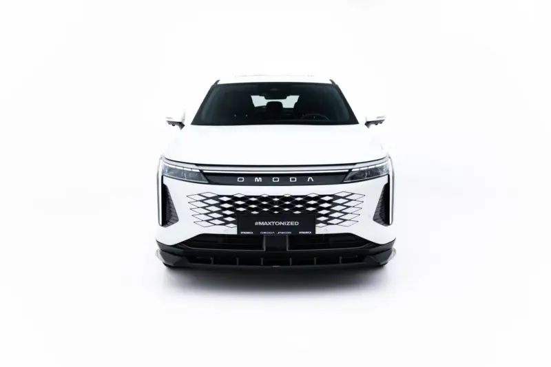 Front view of a white SUV facing the camera in a bright studio; bold grille and dark windshield, plate reads #MAXTONIZED.