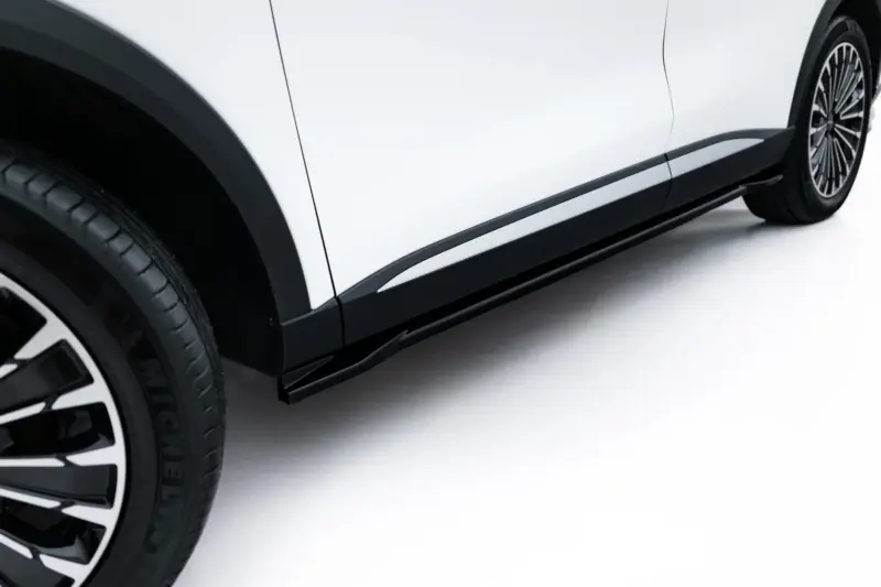 Close-up of a white car's lower side panel with black trim and alloy wheel visible at the edge.