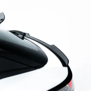 Close-up of a white car's rear end with glossy black trim and red taillight, viewed from a low angle against a white background.