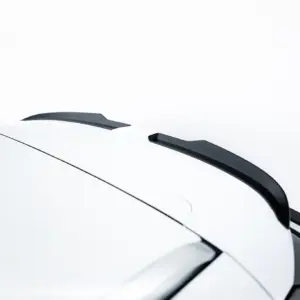 Close-up of a white car roof with a black spoiler and window trim against a pale background.