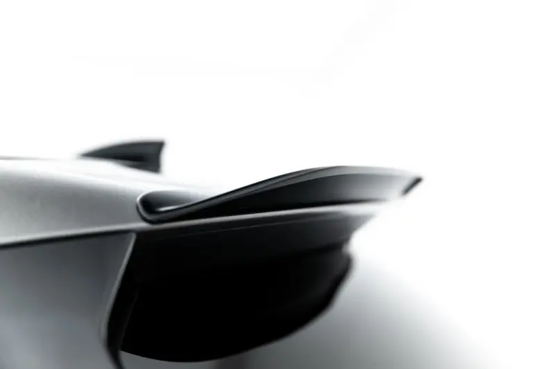 Close-up of a sleek car exterior, showing a chrome trim and curved window against a white background.