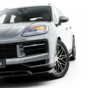 Front-left close-up of a silver Porsche, highlighting the headlight, grille, and stylish alloy wheel with a #MAXTONIZED plate visible on the bumper to left.