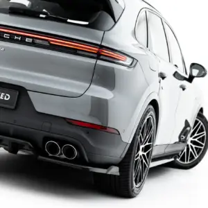Rear view of a silver Porsche Cayenne with illuminated horizontal tail lights and distinctive badging, showing dual exhausts and large alloy wheels at an angle.