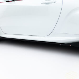Close-up of a white car's side panel and wheel, showing the door, seam, and black alloy wheel with brake caliper visible on the left edge.
