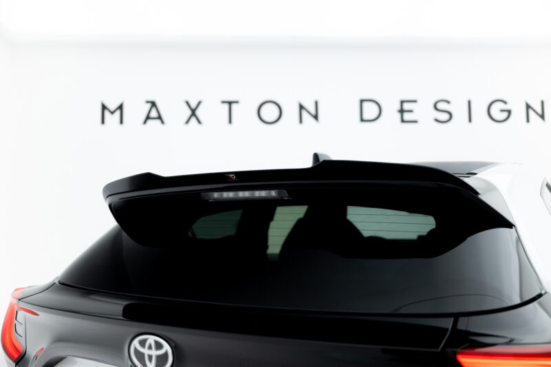 Rear view of a dark SUV with a black spoiler, Toyota badge, and a blurred 'MAXTON DESIGN' sign in the bright background.