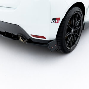 Close-up of a white car's rear quarter panel showing a black alloy wheel, tire, and GR badge on the body.