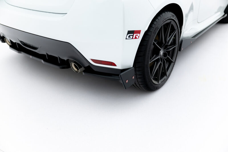 Close-up of a white car's rear quarter panel showing a black alloy wheel, tire, and GR badge on the body.