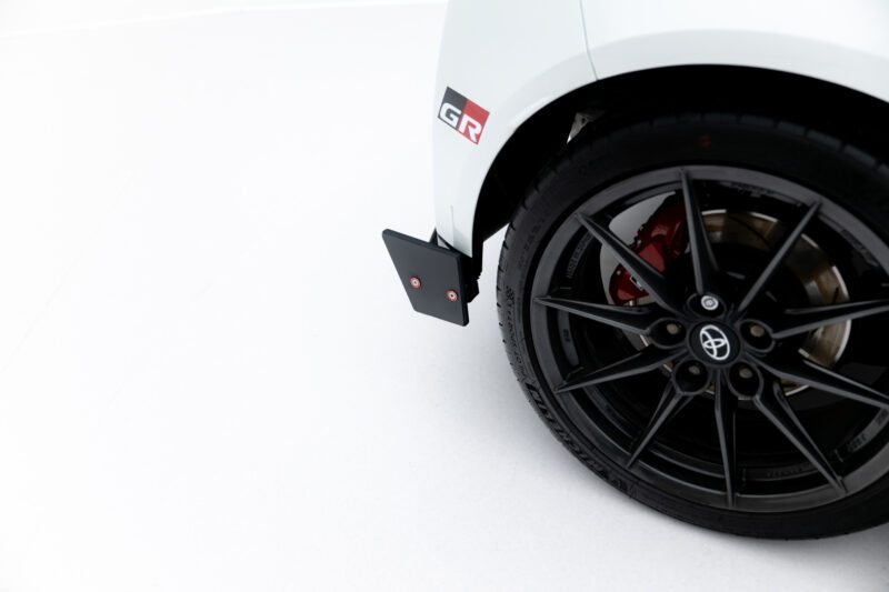 Close-up of a white car wheel with a black alloy rim, red brake caliper, and a GR badge on the fender.